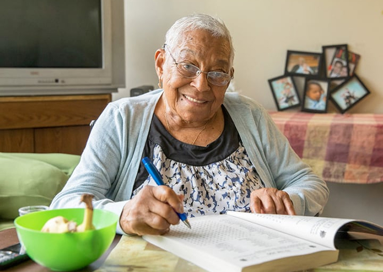 pleased elderly woman working on a crossword puzzle from home